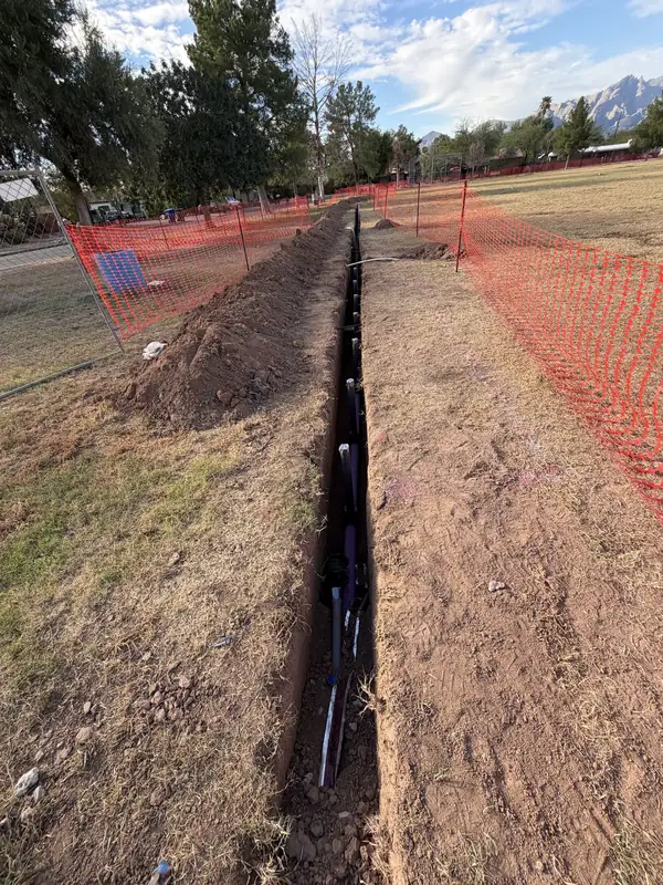 Long irrigation mainline trench running beside orange safety fencing