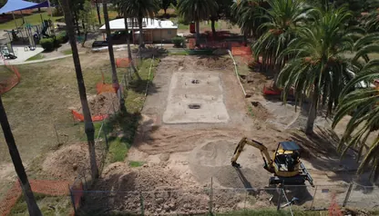 Mini excavator digging inside a fenced work area on a park site